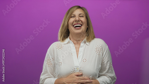 Konstfotografi Woman in white blouse laughing with mouth open and hand on stomach in purple studio; joyful moment