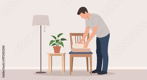 Man folding clean laundry on a chair next to a plant and lamp