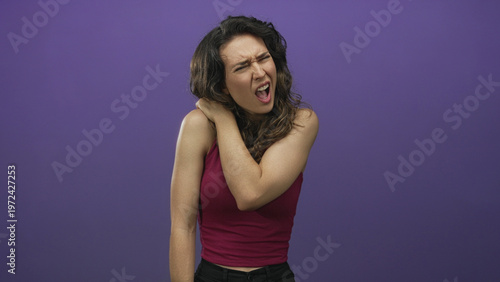 Tableau sur toile Young hispanic woman wearing red tank top holds bare shoulder while wincing in purple studio setting; discomfort