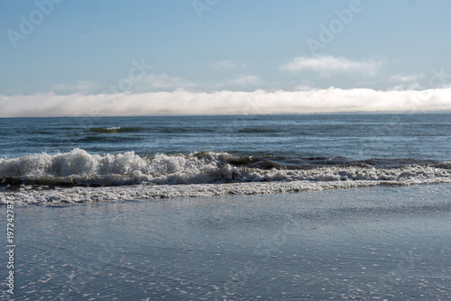 Ocean surf crashing onto sandy shoreline with fog horizon