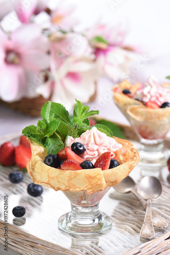 French pancakes with whipped cream filling with strawberries and blueberries, strawberry syrup, almond petals. Served in a glass and garnished with mint.  