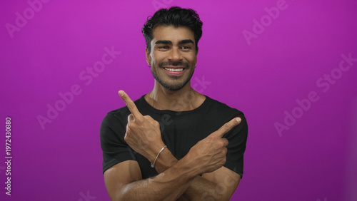 Tableau sur toile Smiling hispanic man crossing arms and pointing index fingers in purple studio setting; choice decision confidence