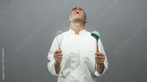 Φωτογραφία Man chef holding whisk and ladle, mouth open and head tilted back in a studio; playful exuberance joy