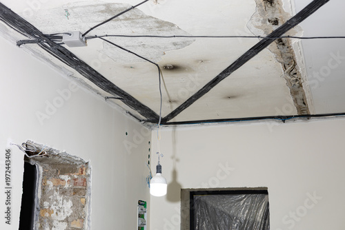 Fotografie House interior during rough renovation and reconstruction, with exposed electrical wires hanging from the ceiling and unfinished walls