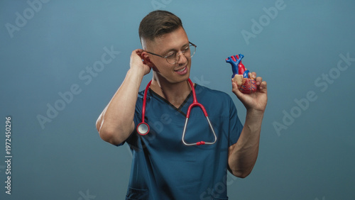Wallpaper Mural Man cardiologist in studio holding anatomical heart model, hand to neck and stethoscope visible; playful curiosity. Torontodigital.ca