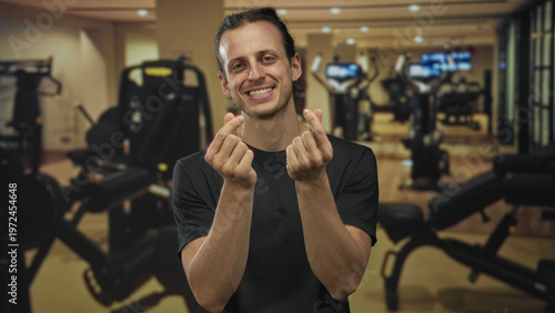 Fotografie Man smiling and showing finger heart with hands in a studio gym setting, long hair visible and forearms bare; joy connection
