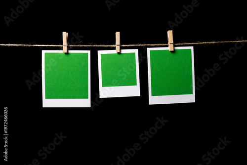 Three green rectangular sheets of paper in a white frame hang from a thin thread against a black background, attached with a clothespin, side view. Space for text