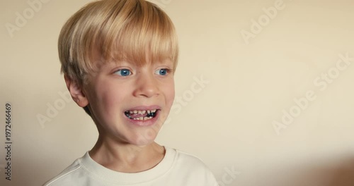 A close-up of a blond boy who smiles sincerely and touches his loose milk tooth with his pointer finger.