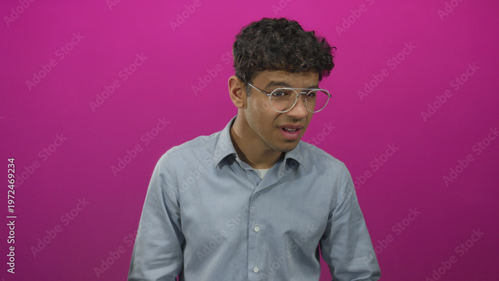 Obraz premium Young hispanic man with scrunched face holding chin with hand against vibrant pink background in studio; thought.