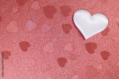A white paper heart lies on a red background with other red hearts. Valentine's Day