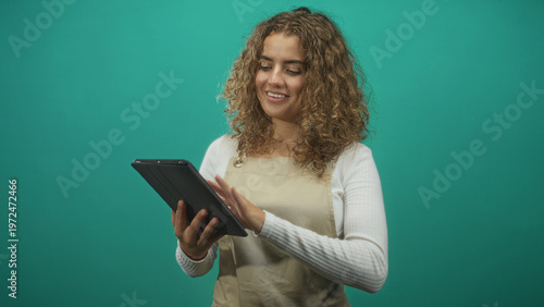 Foto Woman in apron tapping tablet with right hand and holding device with left in studio, smiling while gesturing to screen; digital learning joy
