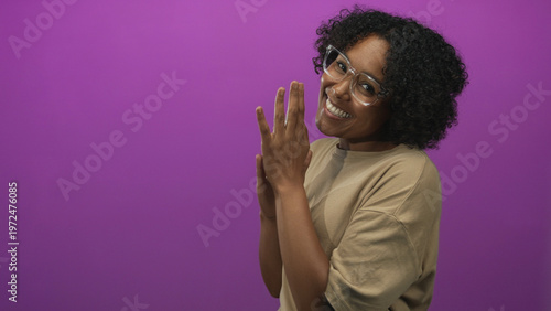 Quadro su tela Woman wearing glasses and a beige shirt with clasped hands and curly hair smiling in studio; joy gratitude