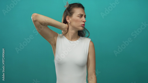 Εκτύπωση καμβά Woman rubbing her neck in studio with teal backdrop and white sleeveless top; discomfort tension fatigue