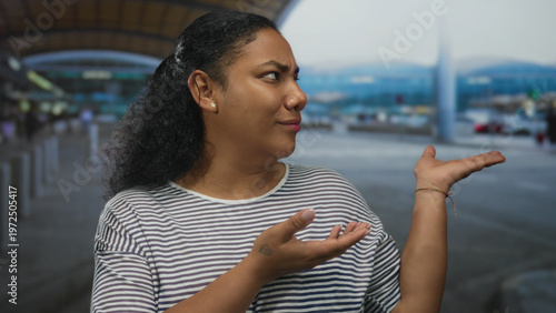 Bilde på lerret African american woman wearing striped shirt holds open palms at airport terminal curbside under canopy; confusion
