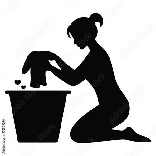 A woman kneeling and washing clothes in a bucket depicted in a striking black silhouette