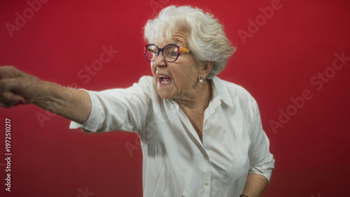 Quadro em tela Elderly woman in white shirt and glasses crosses arms and repeatedly points a finger while scolding in studio; stern reprimand