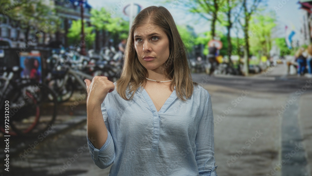 Fototapeta premium Blonde woman pointing thumb to street beside sunlit canal flanked by bicycles in amsterdam; skepticism.