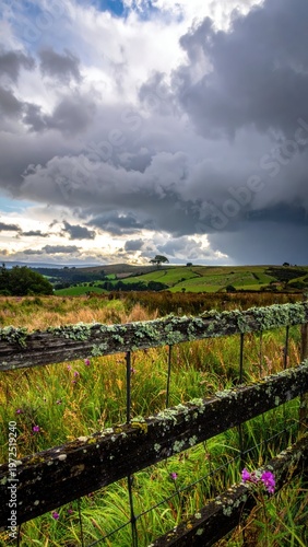 Stormy Sky Over Green Hills and Rustic Wooden Fence Landscape