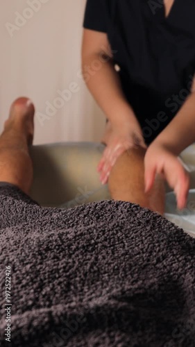 Vertical video of therapist performing sports massage on male leg at clinic