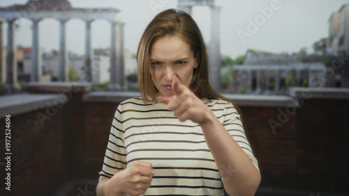 Konstfotografi Young woman points finger directly at camera in ancient roman building; anger tension defiance frustration
