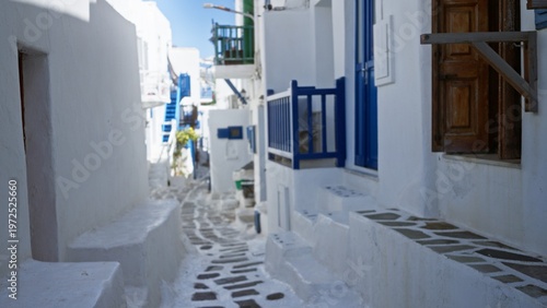 Foto Whitewashed mediterranean alley with blue doors and railings, softly blurred shallow focus on stepped stone pathway and terraces in sunlight; background backdrop copyspace calm