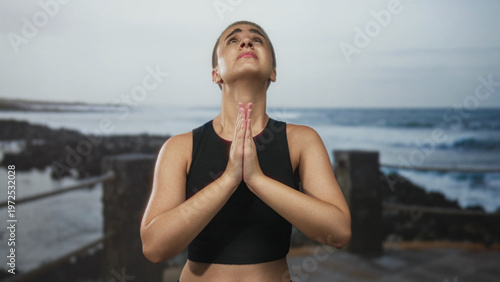 Wallpaper Mural Woman with clasped hands and visible bare shoulders praying and looking upward on a street by the coast with railing and waves visible; sorrow. Torontodigital.ca