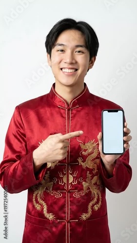 Smiling Asian man in traditional red garment points to smartphone screen, celebrating culture and technology