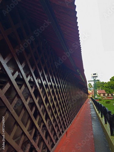 A long, perspective view of a wooden lattice walkway and red-roofed corridor within the Cellular Jail complex.