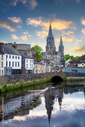 A stunning sunset illuminates the spires of Saint Fin Barre's Cathedral, which reflect beautifully in the calm waters of the River Lee in Cork City.