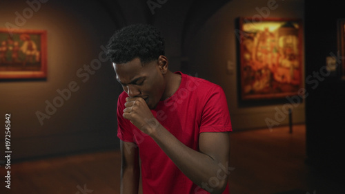 Foto Young african american man in red shirt with hand on cheek for toothache in art gallery building; discomfort