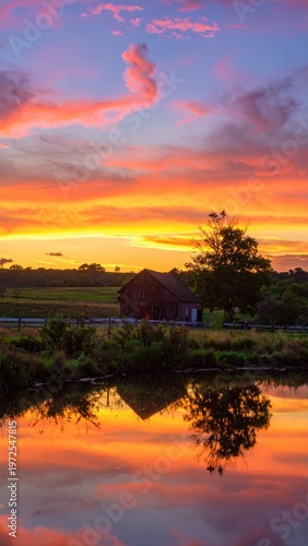 Vibrant Sunset Reflected in Calm Water Near Rustic Barn