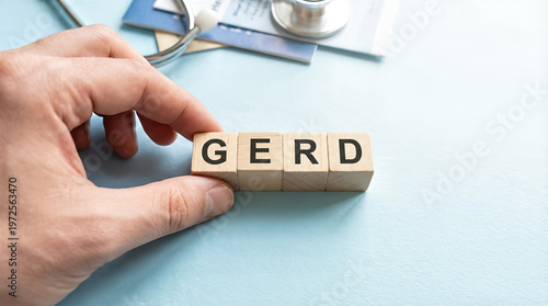 Hand holding wooden blocks with the acronym gerd, standing for gastroesophageal reflux disease, on a light blue background with a stethoscope