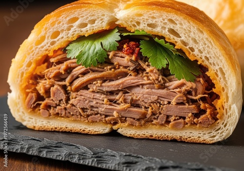 Closeup of a delicious pulled pork sandwich with fresh cilantro and chili flakes on a dark slate board