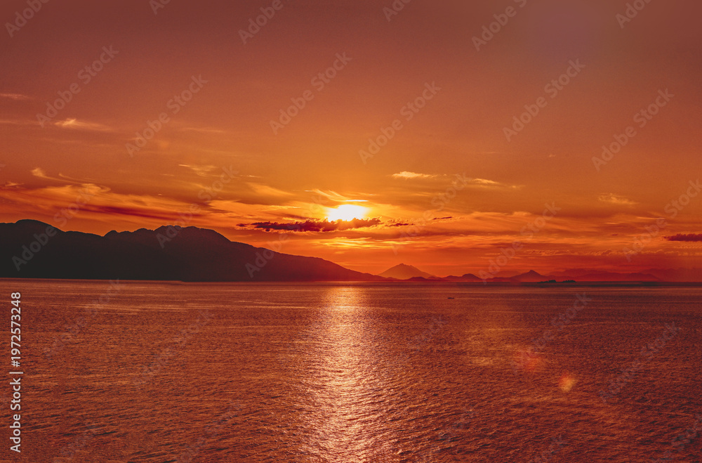 Fototapeta premium Golden Alaskan fjord sunset illuminating calm waters and distant forested mountain silhouettes