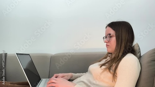 Laptop typing continues as woman on sofa works online at home. Female uses computer during remote job focusing on digital task. Productivity concept for freelance occupation indoors..