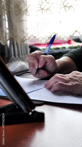 A close-up of the hand of a woman with nail dystrophy writing with a pen in a notebook while sitting at a table.