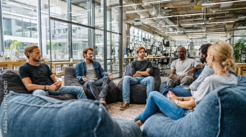 Diverse group of professionals engage in discussion while seated on casual furniture within a modern office space