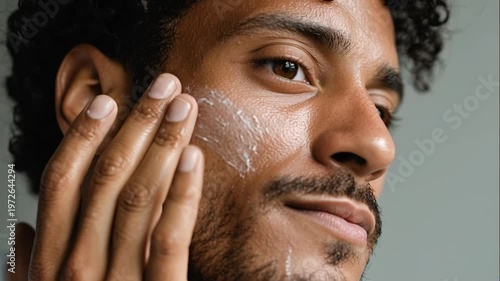 Young man of color applying sunscreen cream on cheek for skin protection