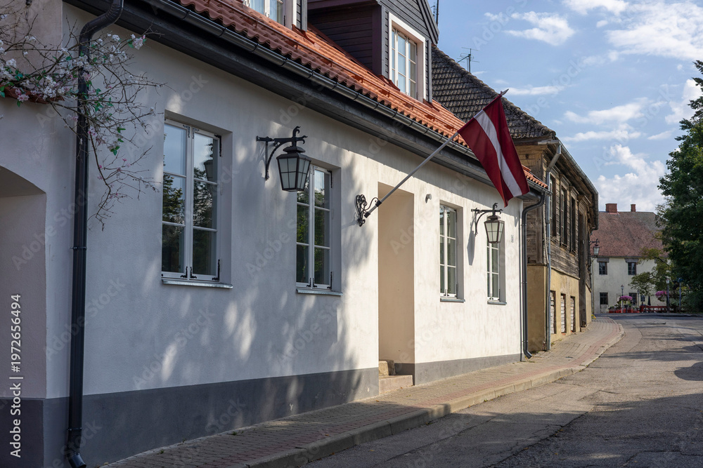 Fototapeta premium Charming street view in Cesis Latvia captures the essence of a peaceful afternoon with a Latvian flag waving gently