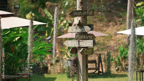 Wooden signpost with directional arrows in green park setting with travel destinations, Rustic outdoor guide with directions to waterfall camping cafe and facilities in natural landscape