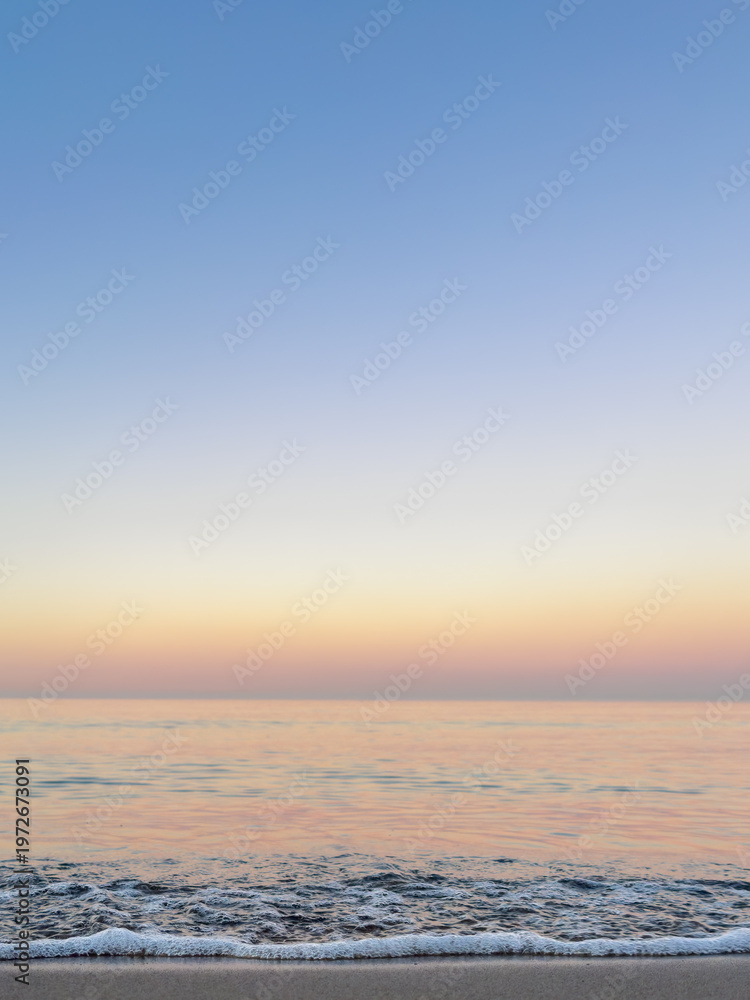Fototapeta premium White sea foam against a pastel sunset sky. Vertical seascape background.