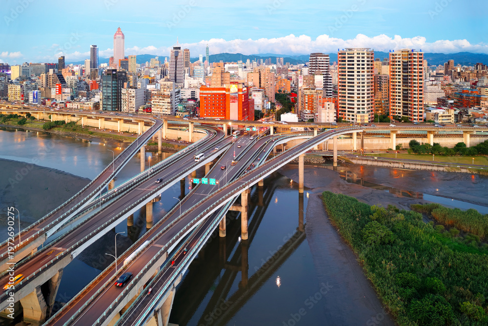 Fototapeta premium Top view of Zhongxing Bridge spanning Tamsui River & connected to the riverside Huanhe Expressway with crowded buildings in Ximending Downtown & 101 Tower standing in background in vibrant Taipei City