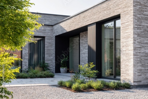 A contemporary house featuring striking brick walls and expansive windows stands proudly in a residential neighborhood, bathed in the warm light of daytime