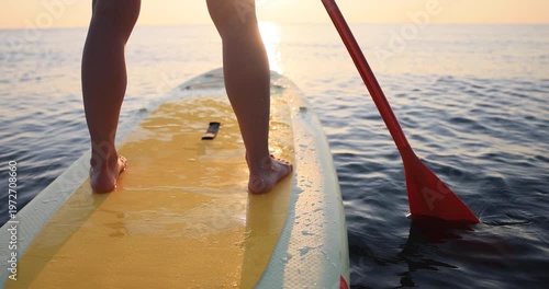 Beautiful women's legs on the SUP board against sunrise background. Slow motion