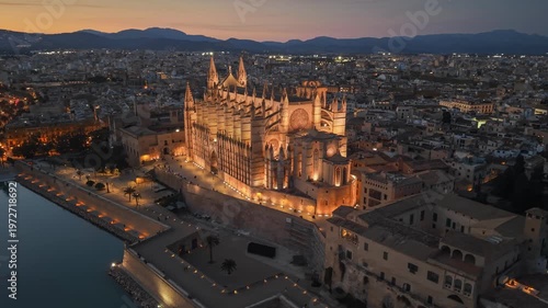 Evening view of the illuminated Cathedral of Santa Maria in Palma, Mallorca aerial footage of the city lights and harbor at dusk. Majestic Palma Cathedral in Mallorca glowing in the evening darkness