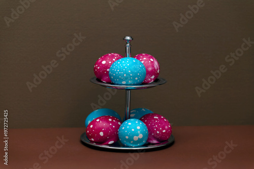 Colorful painted Easter eggs on a two-tier serving stand against a brown background