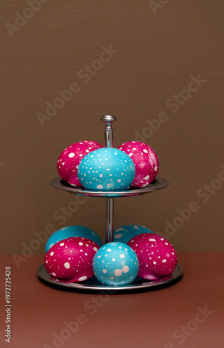 Colorful painted Easter eggs on a two-tier serving stand against a brown background