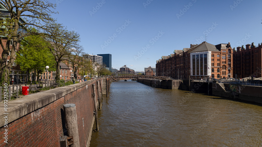 Fototapeta premium View along Hamburg canal with brick warehouses and bridge in Speicherstadt district