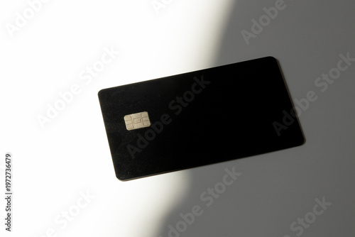 A black bank card with a chip lies on a white background with contrasting lighting and shadow. The theme is payment, banking, security