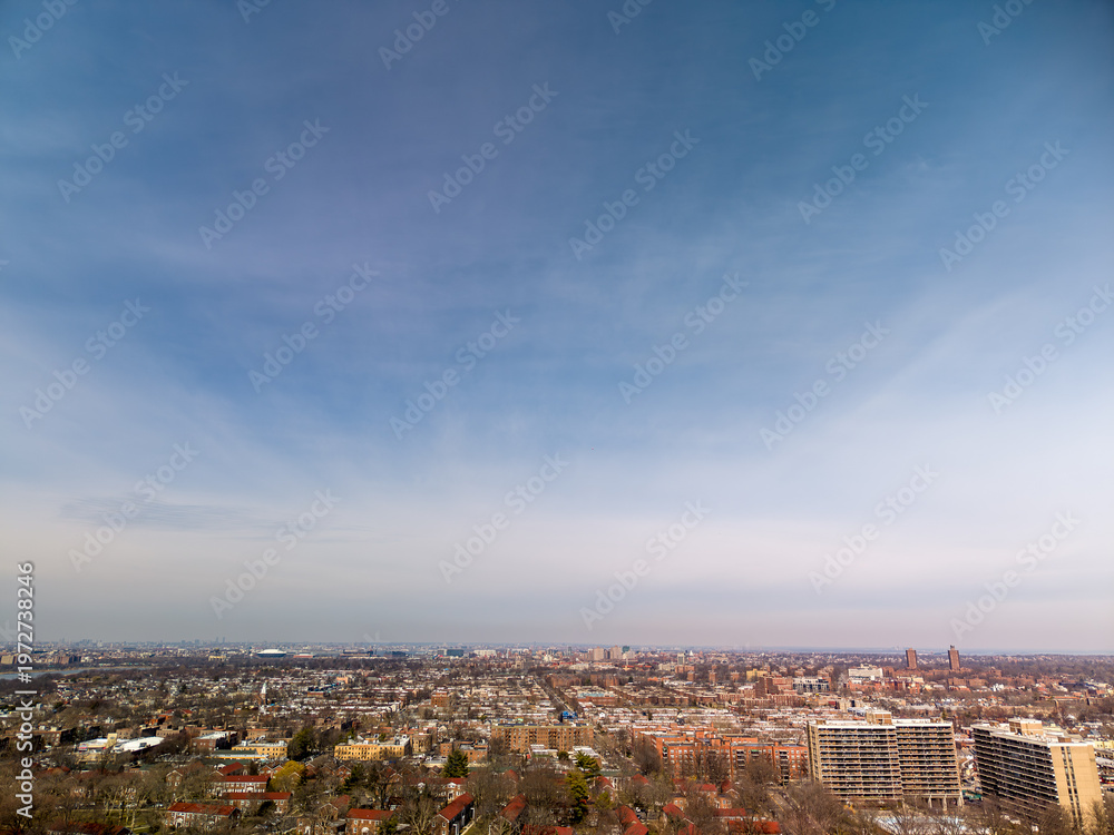 Obraz premium Expansive urban vista showcasing a sprawling residential cityscape with a mix of multistory apartment buildings and individual houses under a wide. Pale blue sky